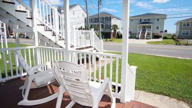 A porch with white rocking chairs and a wooden deck.