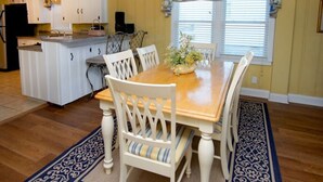 A dining area with a wooden table, white chairs, and a floral window valance.