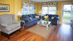 A living room with two blue sofas, a grey armchair, a glass coffee table, and a ceiling fan.