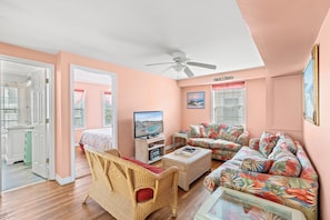A living room with a television, wicker furniture, a ceiling fan, and a floral sofa. - Belair (Up) -  Cherry Grove Channel House with a Pool (North Myrtle Beach)