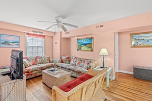 A living room with a sectional sofa, a television, wicker furniture, and paintings on the walls.