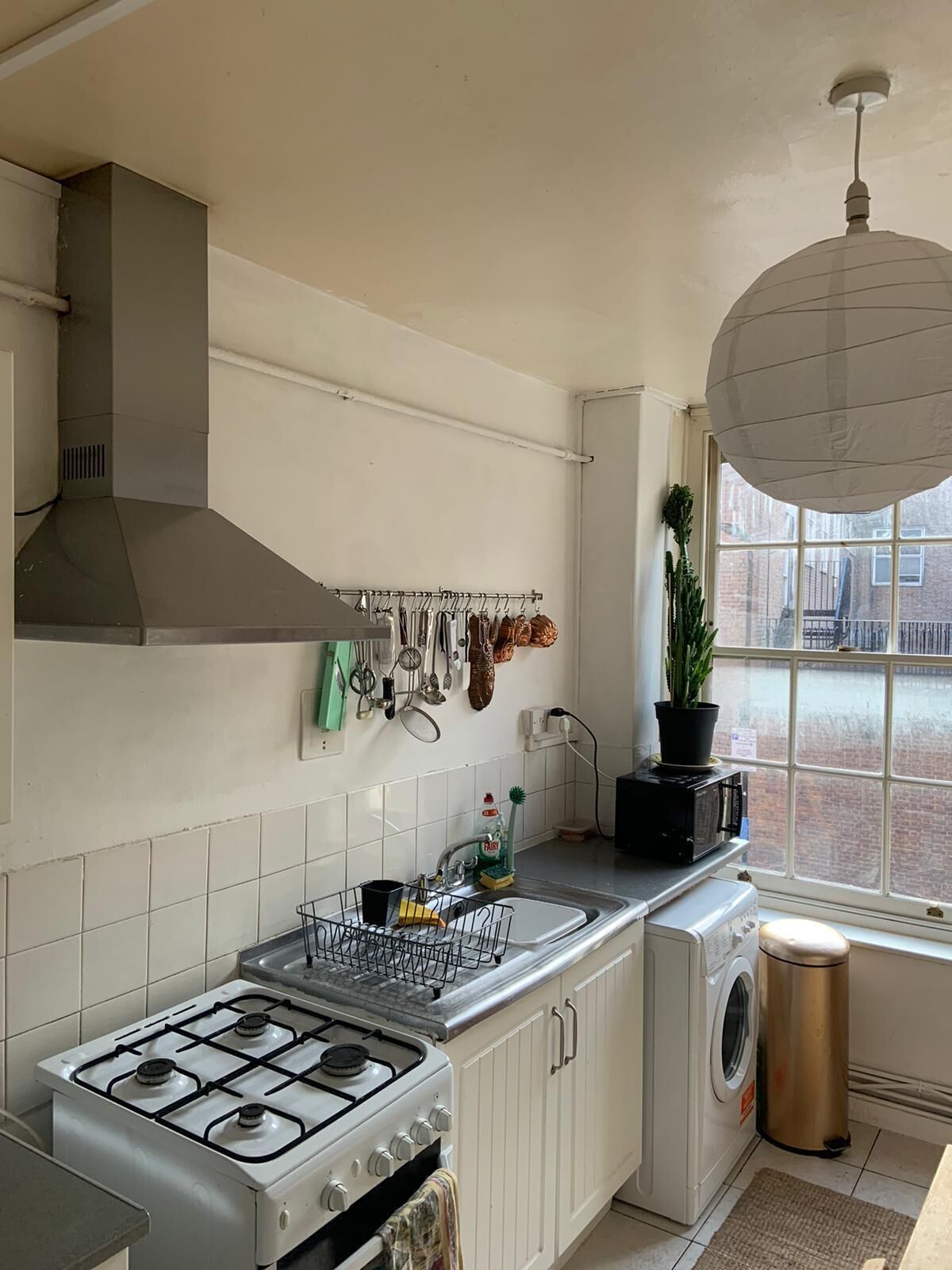 A compact kitchen with a gas stove, a built-in oven, a microwave, a sink, and a window with a view of the city.