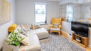 Ein modernes Wohnzimmer mit einem Ecksofa, einem gelben Sessel, einem Flachbildfernseher und einem großen Fenster.