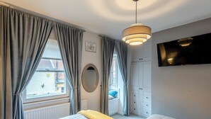 Ein Schlafzimmer mit einem Bett, einer gelben Decke, einem Fernseher und einem Fenster mit Vorhängen.