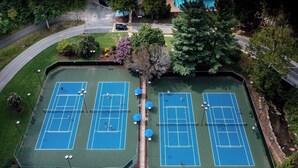 Vue aérienne d’un complexe de courts de tennis comprenant plusieurs terrains, entouré d’arbres et bordé d’une route.