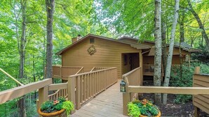 Une cabane en bois dotée d’une terrasse en bois et d’un porche couvert, entourée d’arbres.