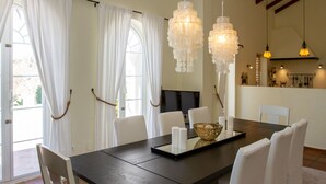 Een eetgedeelte met een donker houten tafel, witte stoelen, een televisie en decoratieve verlichting.