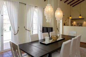 A dining area with a dark wooden table, white chairs, a TV, and decorative lights.
