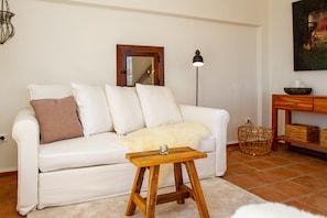 A white sofa with a small wooden table in front, a floor lamp, a basket, and a painting on the wall.