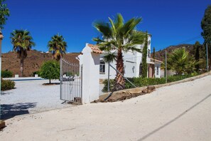 A white building with a gated entrance, palm trees, and a clear blue sky.