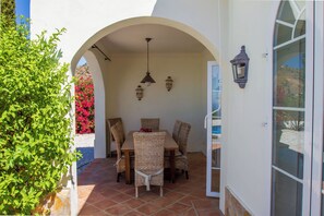 An outdoor patio with a table and chairs, a hanging light fixture, and a wall-mounted lantern.
