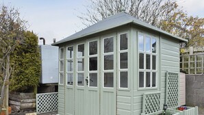 A small, light green shed with multiple windows and a door, surrounded by gravel and wooden fencing. - Och Moo at Number 47 (Seahouses)