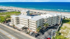Ein mehrstöckiges Hotel mit Parkplatz und Blick auf Strand und Meer.
