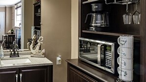 Eine Küche mit dunklen Holzschränken, einer Arbeitsplatte aus Granit, einer Kaffeemaschine, einer Mikrowelle und einem Weinregal.