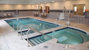 Piscina interna com água cristalina, prancha de mergulho e cadeiras de sol.