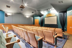 Une salle de théâtre avec des rangées de sièges, un écran et une scène.