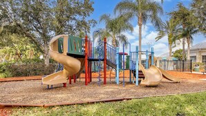 Ein Spielplatz mit Rutschen und Klettergerüsten, umgeben von Bäumen und wolkenlosem Himmel.