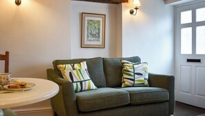 A cozy living room with a green sofa, two wall-mounted lamps, a framed picture, and a door with windows. - 1 bedroom accommodation in Kirkby Lonsdale (Kirkby Lonsdale)