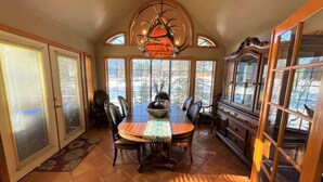A dining room with a large table, chairs, a chandelier, and a view through the windows. - Red River, NM Upper Valley Mountainside Retreat (Red River)