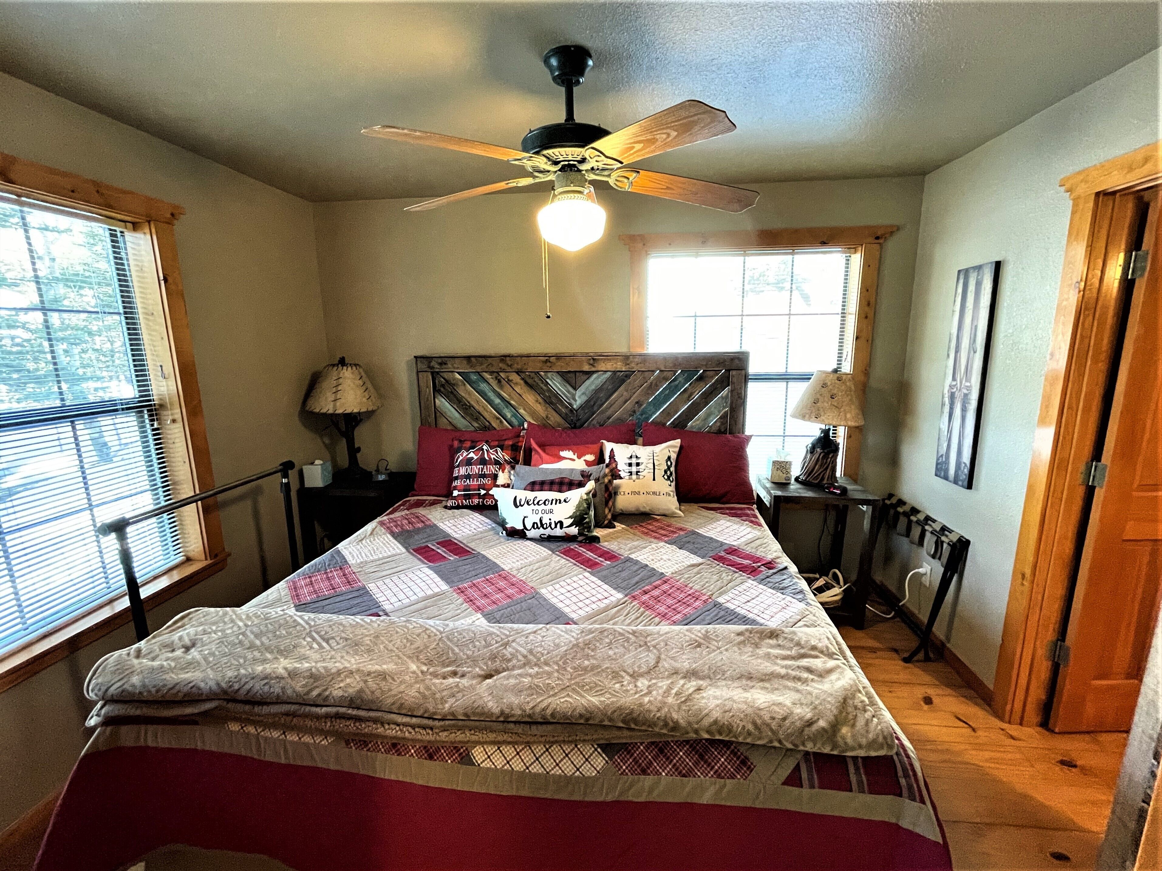 Quarto com cama, ventilador de teto, mesa de cabeceira, luminária e janela com persianas.