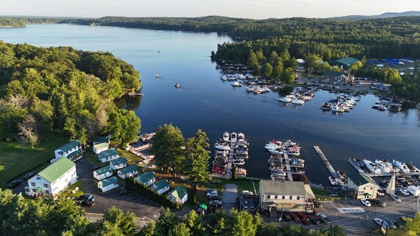 An aerial view of a marina with boats docked, surrounded by dense forest and a small building with a green roof.