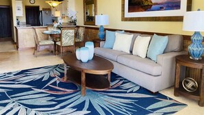 Una sala de estar con un sofá, una mesa de centro y lámparas. Se ve un comedor con sillas y una mesa al fondo.