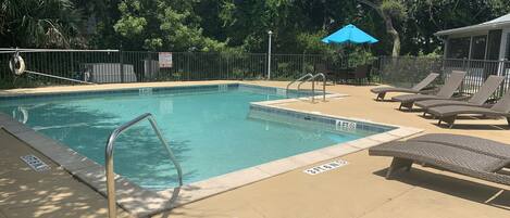 A swimming pool with a safety sign, lounge chairs, and a blue umbrella.