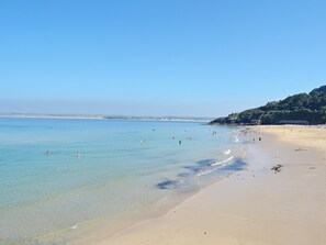 A beach with clear water, a sandy shore, and a hilly landscape in the background.