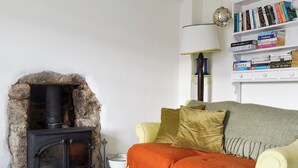 A cozy living room with a stone fireplace, a bookshelf, and a comfortable sofa with a throw blanket. - 2 bedroom accommodation in St Ives (St Ives)