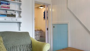 A cozy room with a green armchair, a wooden table, and a bookshelf filled with books. - 2 bedroom accommodation in St Ives (St Ives)