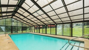 Une piscine intérieure dotée d’un toit en verre et entourée de fenêtres.