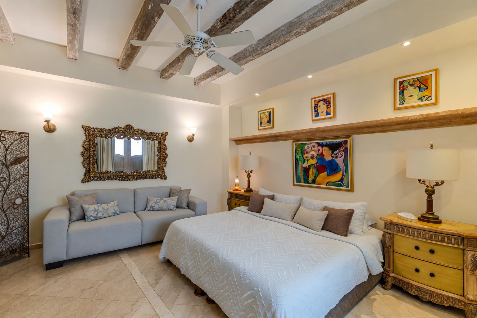 A bedroom with a bed, a sofa, a nightstand, a lamp, and wall art.