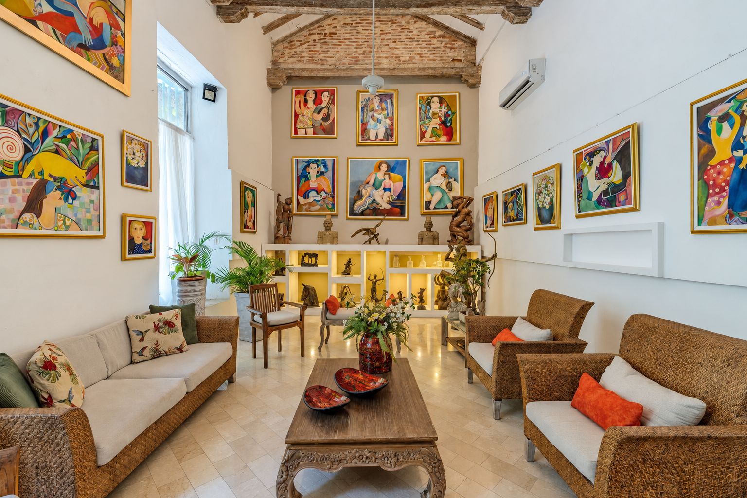 A spacious living room with a high ceiling, multiple seating areas, and a variety of artwork on the walls.