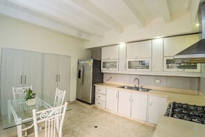 Una cucina moderna con mobili bianchi, un frigorifero in acciaio inossidabile, una stufa a gas e un tavolo da pranzo in vetro con sedie.
