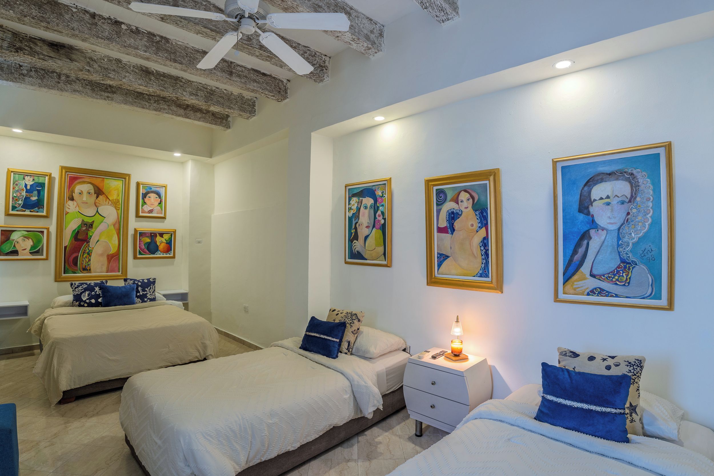 A hotel room with two beds, a nightstand, and artwork on the walls.