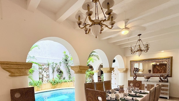 Comedor con vista a la piscina, con una mesa dispuesta para cuatro personas, ventanas de arco y una araña.