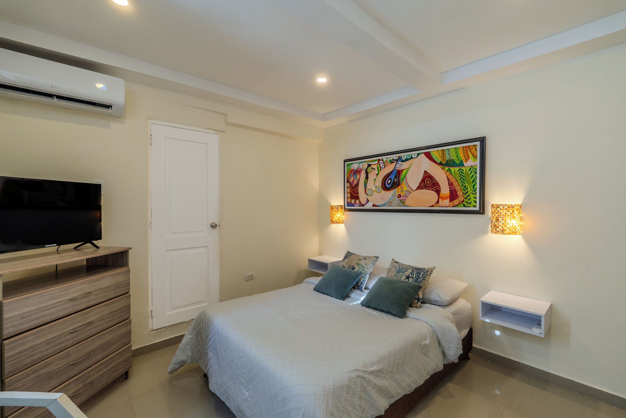 Quarto com cama, televisão, cómoda e um quadro na parede.