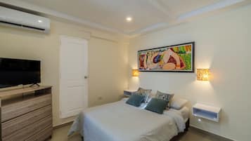 Quarto com cama, televisão, cómoda e um quadro na parede.