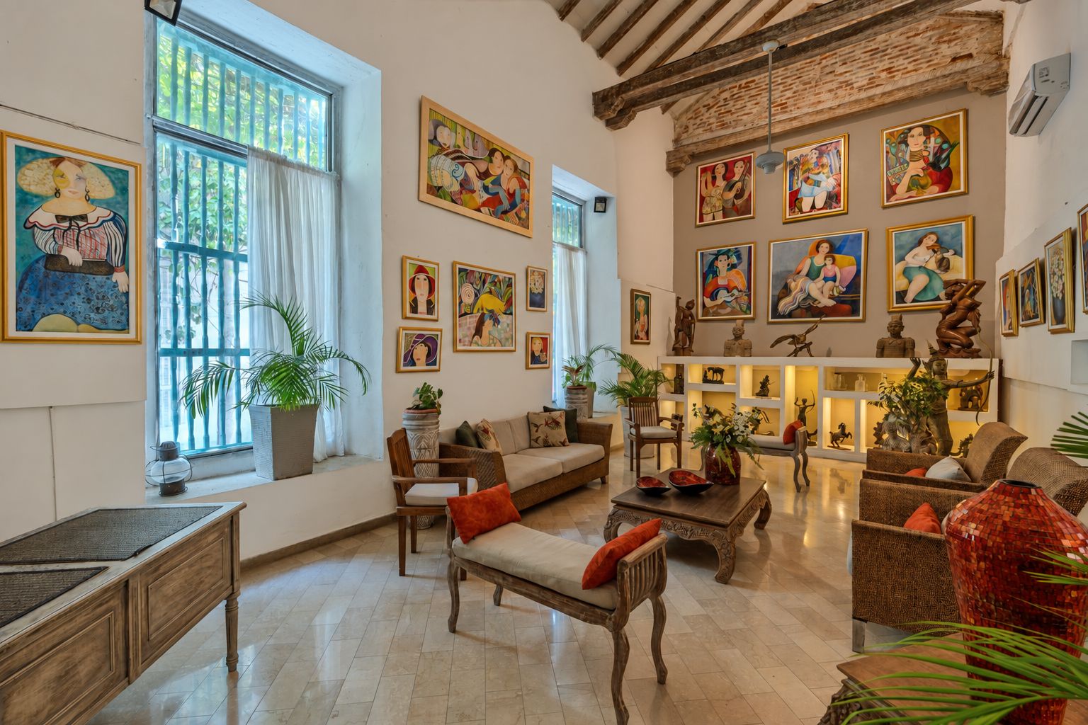 Uma sala de estar ampla, com pé direito alto, janelas grandes e diversas obras de arte nas paredes.