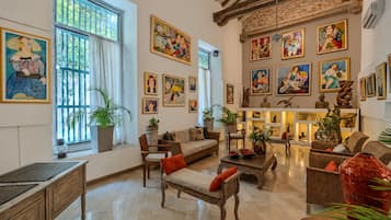 Uma sala de estar ampla, com pé direito alto, janelas grandes e diversas obras de arte nas paredes.