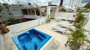 Una azotea con un jacuzzi azul, sillones de descanso y plantas en macetas.