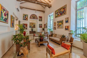 A spacious living room with a high ceiling, wooden beams, and a large window.