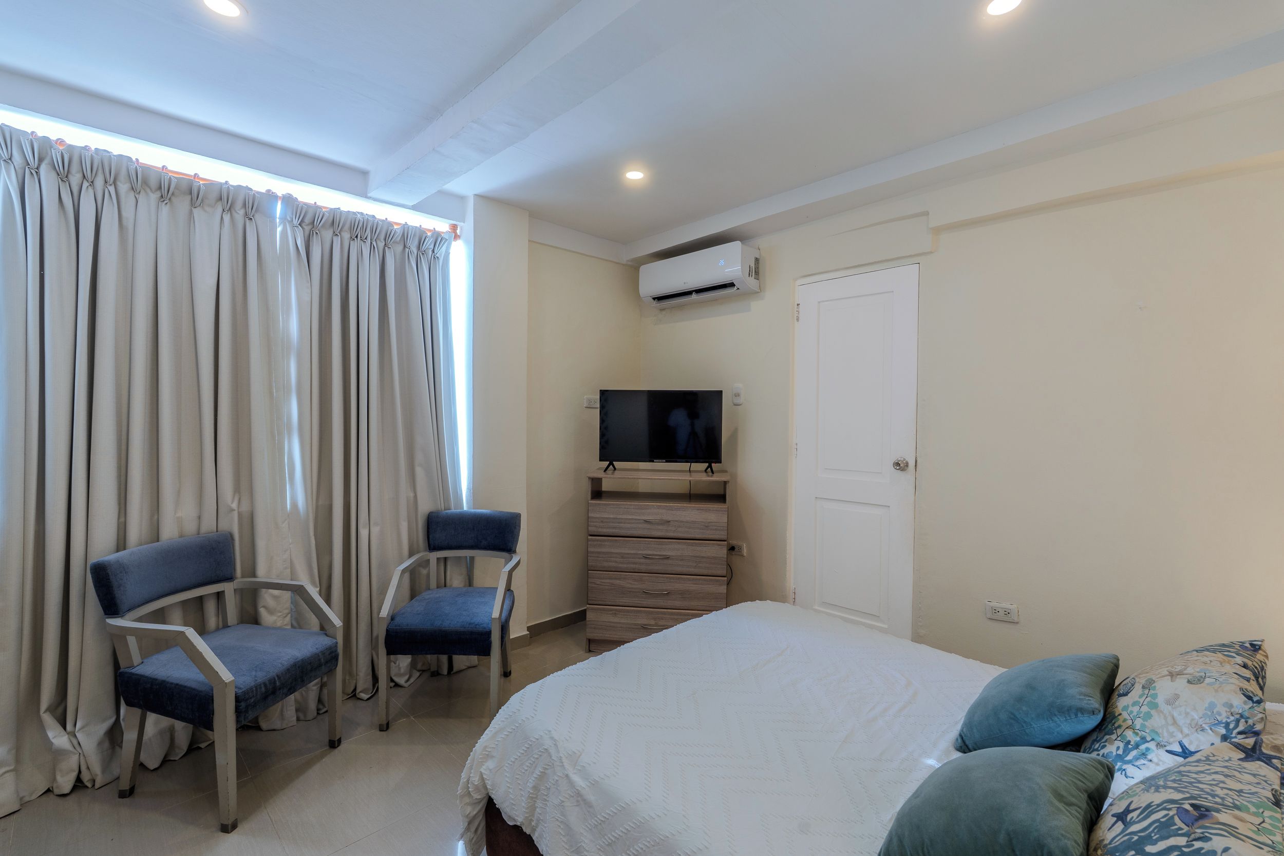 Een slaapkamer met een bed, twee stoelen, een televisie en een airconditioning.
