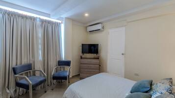 Een slaapkamer met een bed, twee stoelen, een televisie en een airconditioning.