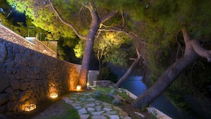 Un sendero de piedra que conduce a una terraza de madera, con un muro de piedra a un lado y una masa de agua al otro.