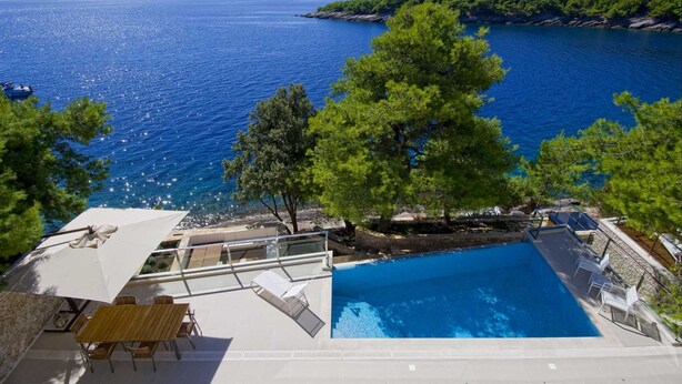 Zona junto a la piscina con vista al mar, una mesa de madera y sillones de descanso.