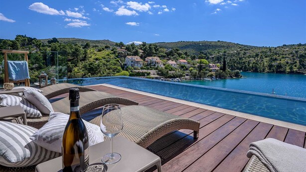 Área de piscina com mobiliário de vime, uma garrafa de vinho e um copo.