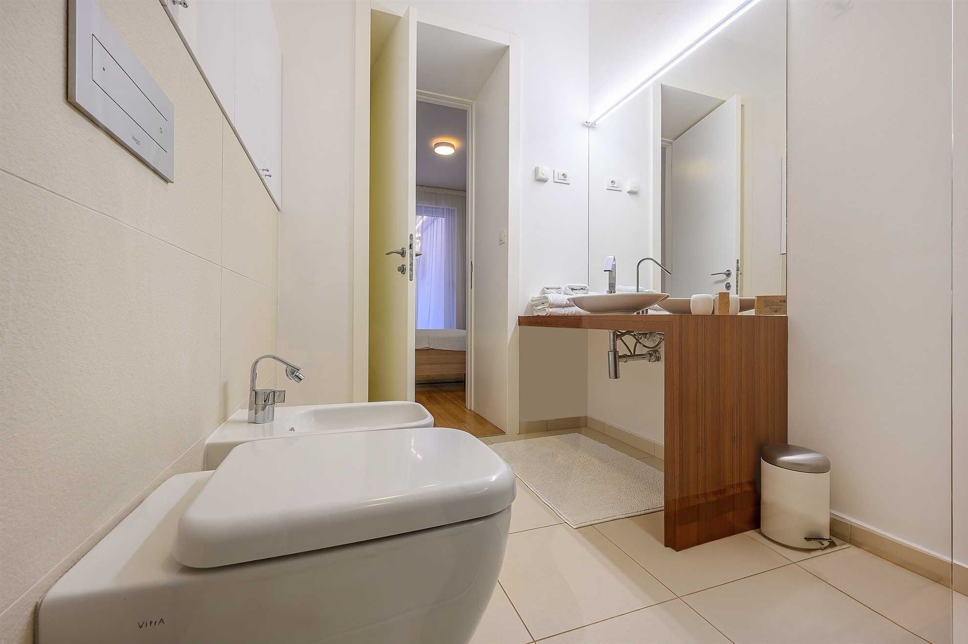 Une salle de bain moderne avec un lavabo blanc, des toilettes et un miroir au-dessus du lavabo.