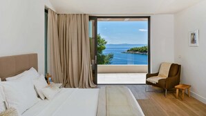 A bedroom with a bed, a chair, a small table, and a view of the sea through a glass door. - Luxury Villa Notturno with Infinity Pool (Selca)