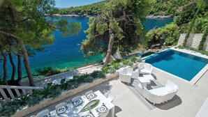 A poolside area with a dining table set for six, overlooking a clear blue sea and surrounded by trees. - Luxury Villa Notturno with Infinity Pool (Selca)